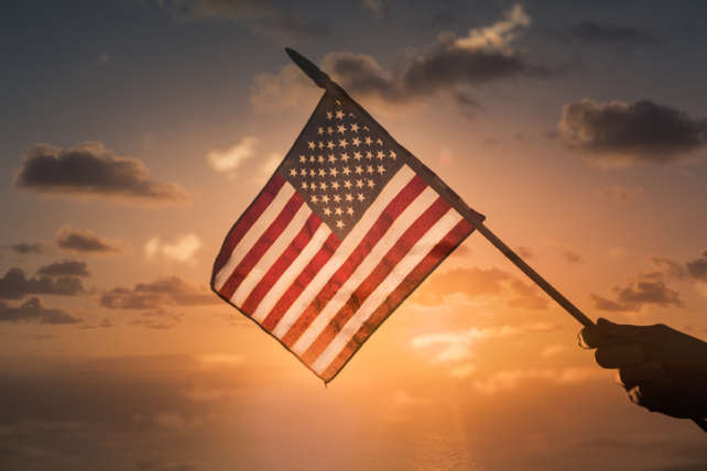 Person holding USA American flag on sunset background.